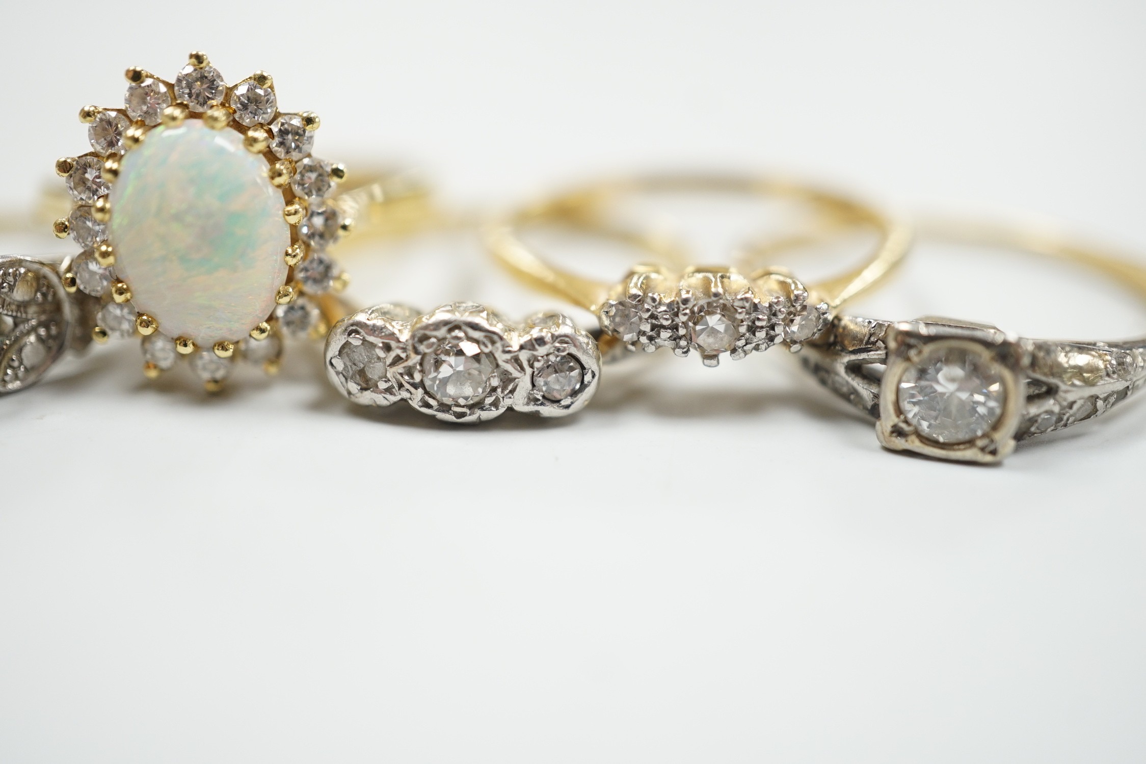 Four assorted 18ct and gem set dress rings, including white opal and diamond and two three stone diamond and one yellow metal and single stone diamond set ring, gross weight 14.3 grams.